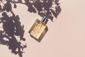 un elegante botella de cosmético rociar o perfume en un ligero antecedentes entre el sombra de árbol sucursales. luz de sol. Copiar espacio. parte superior vista. foto
