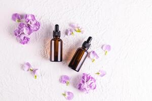Top view of cosmetic bottles made of dark glass with a pipette with a natural facial skin care product. . Flat lay. White background, flowers. photo