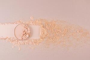 A block of compact powder in a natural tone with the texture of broken pieces stands on a swatch of powder. loose powder. A copy space. top view. photo