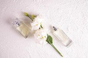 dos diferente botellas de De las mujeres perfume con un floral fragancia en un blanco texturizado antecedentes entre flores parte superior vista. plano poner. perfume concepto foto