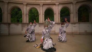 Traditional Japanese dancers in motion, wearing masks and patterned costumes, performing in a courtyard with classical architecture. video