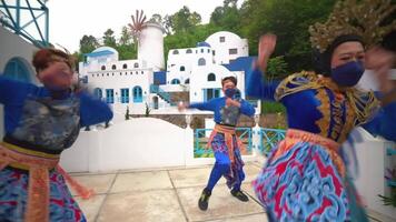 Performers in vibrant traditional costumes dancing at a cultural event with a Mediterranean-style video