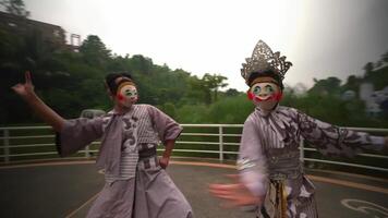 twee artiesten in traditioneel maskers en kostuums poseren buitenshuis met een natuurlijk, groen backdrop video