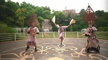 Tres individuos ejecutando un danza rutina al aire libre en un estampado acera, con lozano verdor y arquitectónico estructuras video