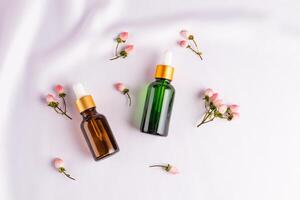 Two different bottles with a dropper with serum or a cosmetic natural face and body care product on white satin among decorative berries. Top view. photo