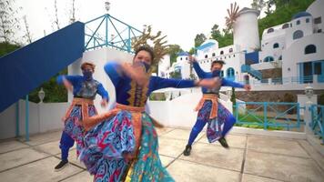 Performers in vibrant traditional costumes dancing at a cultural event with a Mediterranean-style video