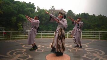 intérpretes en tradicional asiático atuendo y mascaras atractivo en un cultural danza al aire libre, con lozano verdor y un antiguo edificio video