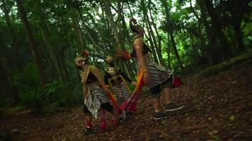 tradicional balinés bailarines en florido disfraces ejecutando en un lozano bosque, exhibiendo cultural patrimonio con un movimiento difuminar efecto video