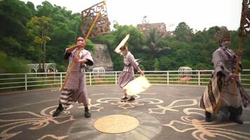 Three individuals performing a dance routine outdoors on a patterned pavement, with lush greenery and architectural structures video