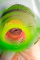 The child's eye looks through the orange-green dense, colorful flexible children's toy, fun plastic toy. Teen girl plays slinky photo