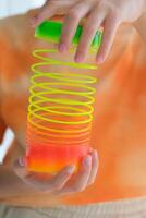 Child playing orange and green tight, colorful flexible children's toy, fun plastic toy. Teen girl plays slinky photo