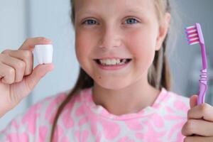 el niño sostiene un el plastico Leche diente y un cepillo de dientes en su manos. el concepto de cepillado y cuidando para dientes. foto