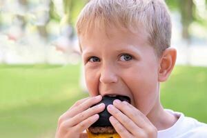 el niño come un negro hamburguesa en el calle. el chico picaduras apagado piezas de un hamburguesa con queso. rápido comida foto