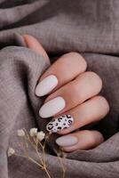 Woman's hand with a beautiful oval-shaped manicure. Autumn trend, beige color polishing with leopard pattern on nails with gel polish, shellac. photo