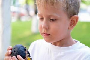 The child eats a black burger on the street. The boy bites off pieces of a cheeseburger. Fast food photo