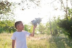 pequeño chico corriendo con un juguete cohete en un puesta de sol campo de verano naturaleza. para niños grande sueño, vuelo, astronauta, espacio, éxito líder ganador concepto foto