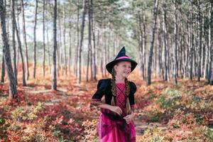 un niña en un bruja disfraz en el bosque. Víspera de Todos los Santos niño vestido como un bruja con cara pintura foto