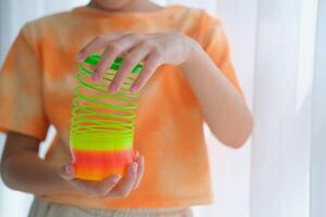 Child playing orange and green tight, colorful flexible children's toy, fun plastic toy. Teen girl plays slinky photo