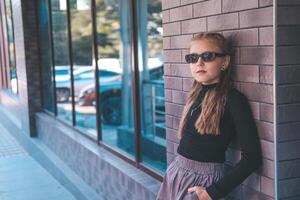 Beautiful teenage girl in stylish clothes on the street. Street fashion, fashionable child wearing sunglasses. photo