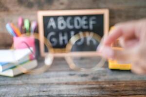 Blurred photo of a hand holding glasses on a background of school supplies. Eye problems, loss of vision.