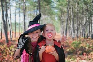 Funny kids in carnival costumes outdoors. A girl dressed as a witch and a boy in a Halloween costume scare looking at the camera. photo