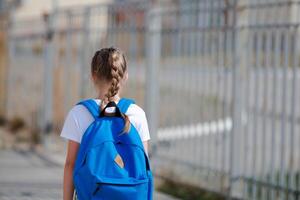 un Chica de escuela niña con un maletín en su espalda va a escuela. espalda a escuela. foto