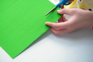 Children's hands cut green paper with scissors. Step-by-step instructions for the craft. Do it yourself concept. Step-by-step photo instructions. Step 7.