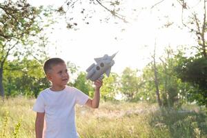 pequeño chico corriendo con un juguete cohete en un puesta de sol campo de verano naturaleza. para niños grande sueño, vuelo, astronauta, espacio, éxito líder ganador concepto foto