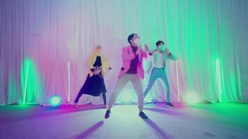 Three young adults dancing on stage with colorful stage lights and a white curtain backdrop video