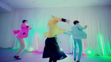 Group of young people dancing energetically in a room with colorful lighting and a white backdrop, showcasing movement and fun. video