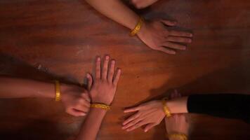 Top view of four people's hands on a wooden table, each wearing yellow friendship bracelets, symbolizing unity and friendship. video