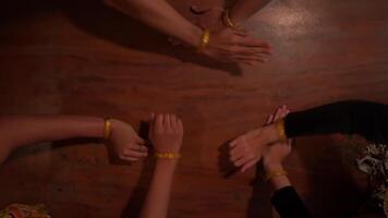 Top view of a diverse group of people joining hands with yellow wristbands on a wooden surface, symbolizing unity and teamwork. video