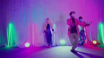 Diverse group of people dancing with face masks in a room with colorful lights and white curtains, depicting safe social activities video
