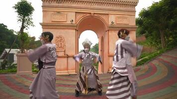 Three individuals in traditional Japanese attire and face masks perform a dance in front of a replica of the Arc de Triumph video