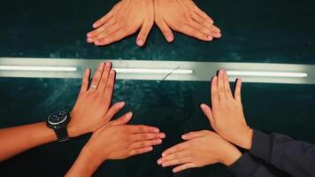 Top view of diverse hands reaching towards each other over a dark reflective surface with a linear light source video