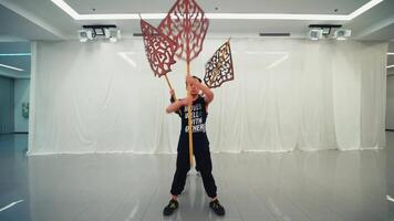 Three individuals holding intricate cut-out designs on poles, partially obscuring their faces, in a modern dance studio video