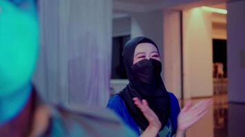 Smiling woman in a hijab engaging in a friendly conversation indoors with colorful lighting video