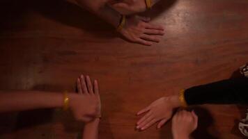 Top view of four people's hands on a wooden table, showing unity and teamwork. The hands are adorned with yellow wristbands video