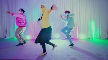 Three people dancing joyfully at a party with colorful stage lights in the background video