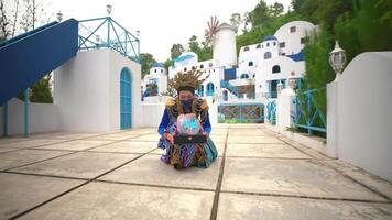 Person in colorful attire holding a tablet in front of a picturesque white and blue building, reminiscent of Mediterranean architecture video