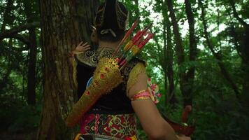 Traditional archer in vibrant costume with a quiver full of arrows, standing in a lush green forest, showcasing cultural heritage video