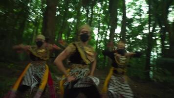 Three performers in traditional masks and costumes dancing in a lush green forest, showcasing cultural heritage video