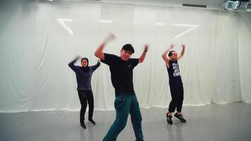 tre diverso persone praticante un' danza routine nel un' luminosa studio con bianca muri, esprimendo gioia e energia attraverso loro movimenti. video