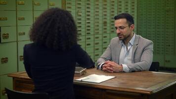 A man and a woman share a conversation at a table, collaborating on a job event video