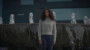 retrato do jovem mulher com Preto encaracolado cabelo dentro a cidade dentro lento movimento video