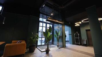 Modern hotel lobby entrance, A stylish hotel lobby entrance with large glass doors and indoor plants, showcasing contemporary interior design and welcoming atmosphere. video