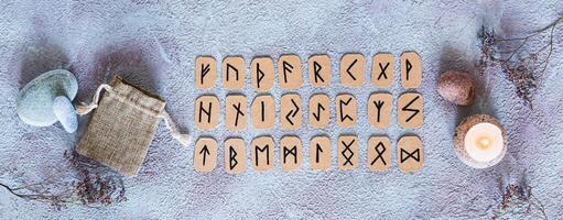 Scandinavian runes for fortune telling, pouch and candle on the table top view web banner photo