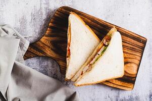 Close up of appetizing sandwich with chicken breast, tomatoes, lettuce and sauce on a board top view photo