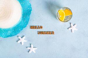 Concept hello summer text, hat, cocktail with orange and starfish on blue background top view photo