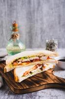 Appetizing sandwich with chicken breast, tomatoes, lettuce and sauce on a board vertical view photo